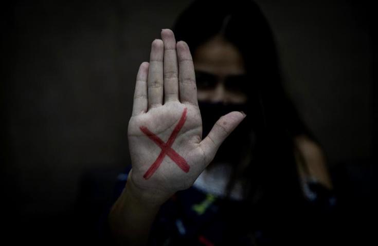 fotografia mostra mulher exibindo a palma de uma das mãos com um "x" vemelho pintado sobre ela