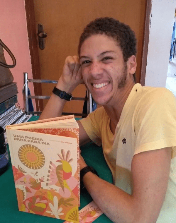 Poeta Galosi sorri com uma mão encostada na cabeça e a outra próxima ao livro "Uma poesia para cada dia".