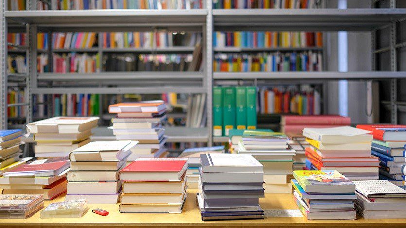 Livros em estantes e em cima de uma mesa. Aparenta ser uma livraria