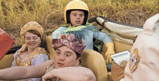 Três jovens com síndrome de down em um carro. Estão usando roupas circenses .