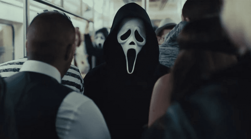 Ghostface, pessoa usando máscara de fantasma e um manto preto, está com várias pessoas ao seu redor no metrô de Nova York.