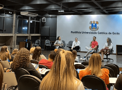 Público e palestrantes no primeiro dia da segunda edição do Simpósio Multidisciplinar do Transtorno do Espectro Autista, em Goiânia. Na foto, costas de pessoas sentadas em cadeiras, de frente para o palco, onde se encontram quatro pessoas conversando. Ao fundo, a logo e o escrito da Pontifícia Universidade Católica de Goiás.

(Foto: Acervo LaTEA/Nathalia Soares Vidiz)
