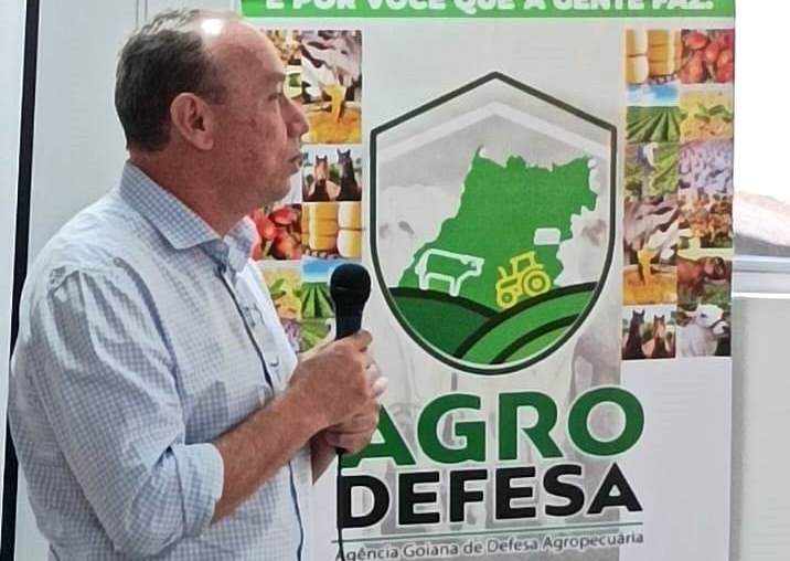 Novo presidente da Agrodefesa, José Caixeta em posse. Homem branco, idoso, em pé, segurando um microfone e com um poster escrito Agrodefesa atrás dele. Gripe aviaria