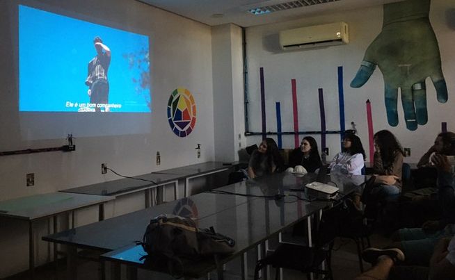 Pessoas assistindo a cena do filme "Aftersun" que está sendo projetada na parede.