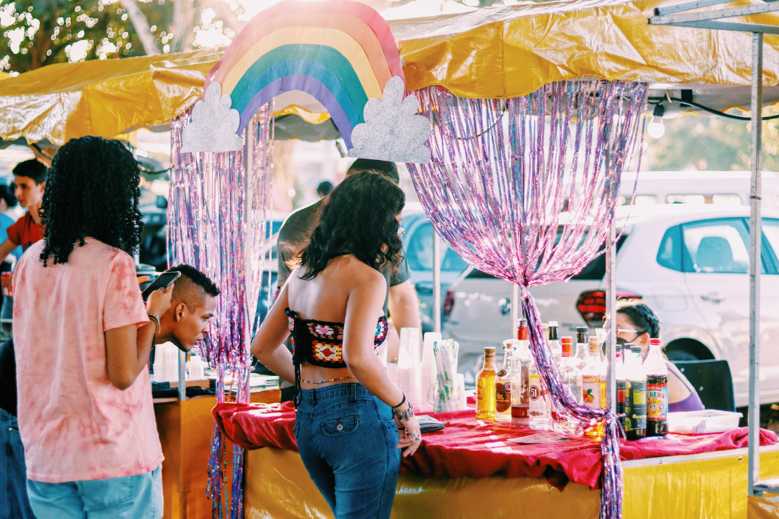 Foto de pessoas observando uma banca com arco-irís na fachada