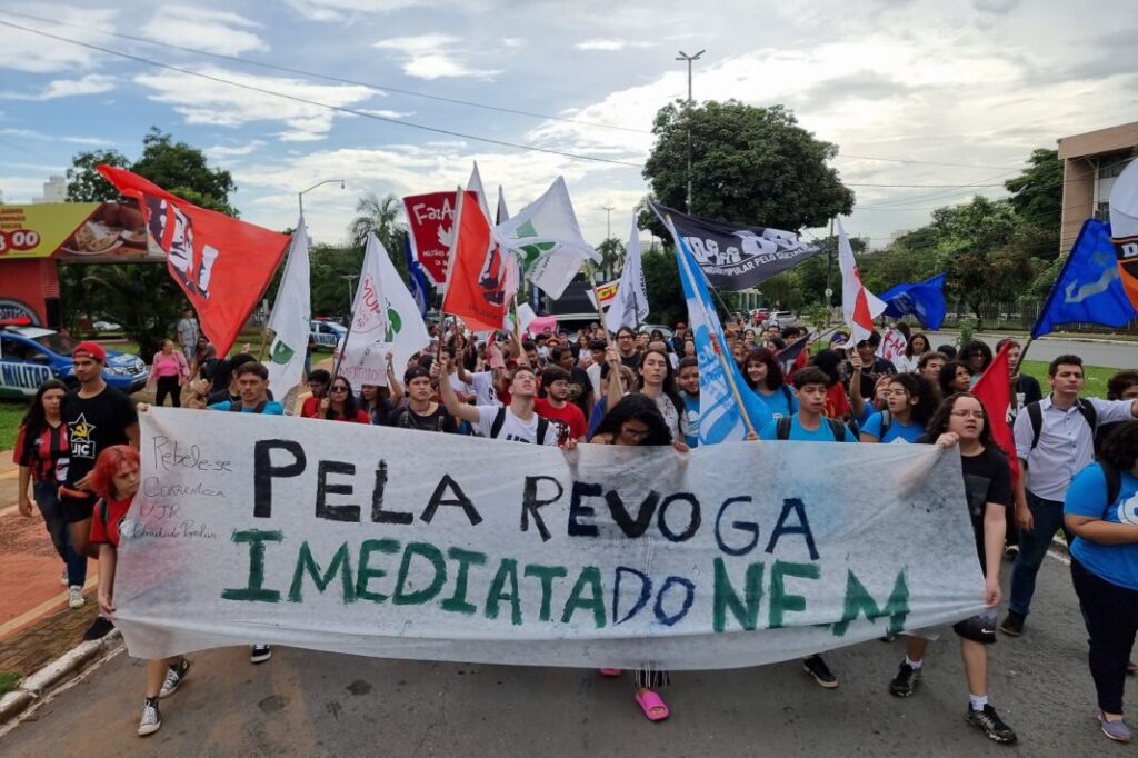Estudantes vão às ruas de Goiânia em manifestação contra o Novo Ensino Médio, em 2023. Na imagem, jovens de várias idades caminham com bandeiras, bandeirões, faixas e cartazes expressando sua insatisfação com o Novo Ensino Médio. (Foto: Rubens Salomão)