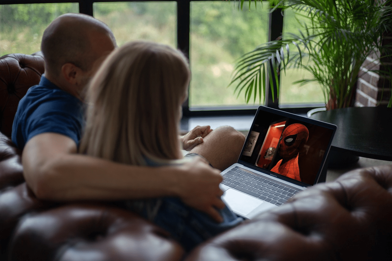 Casal sentado em sofá assistindo o filme do Homem-Aranha no computador. Foto: Frank Reppold via Pixabay.