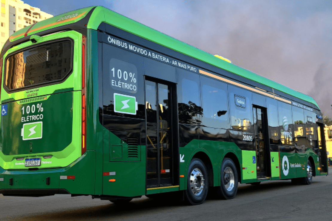 Ônibus elétrico verde e preto com céu azul e fumaça