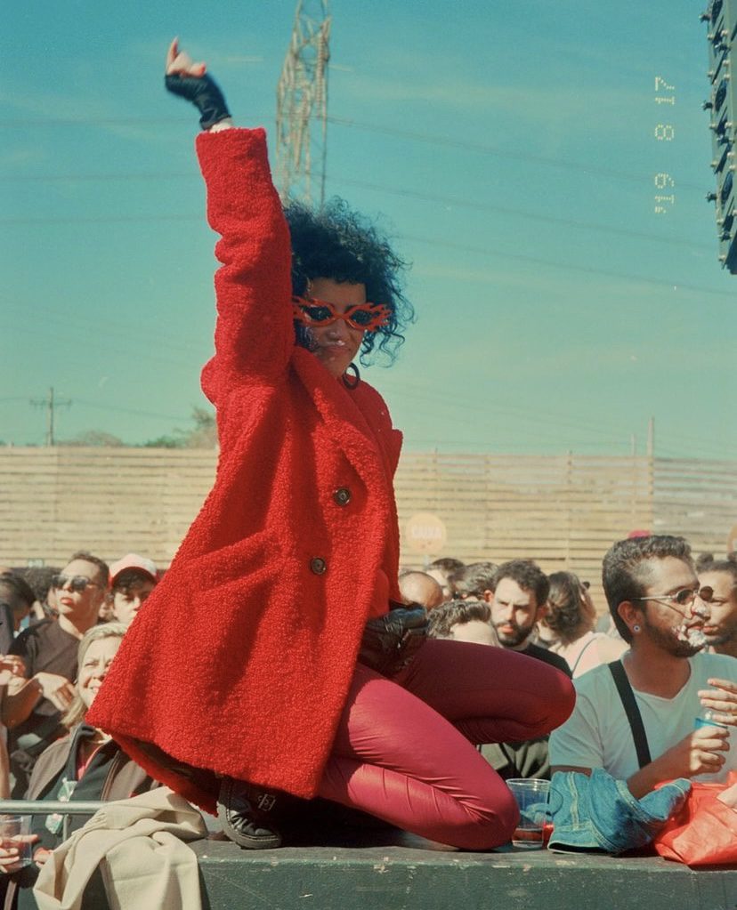 essa foto foi tirada por pedro pinho em belo horizonte e nela temos uma mulher de casaco vermelho com o braço levantado em pose
