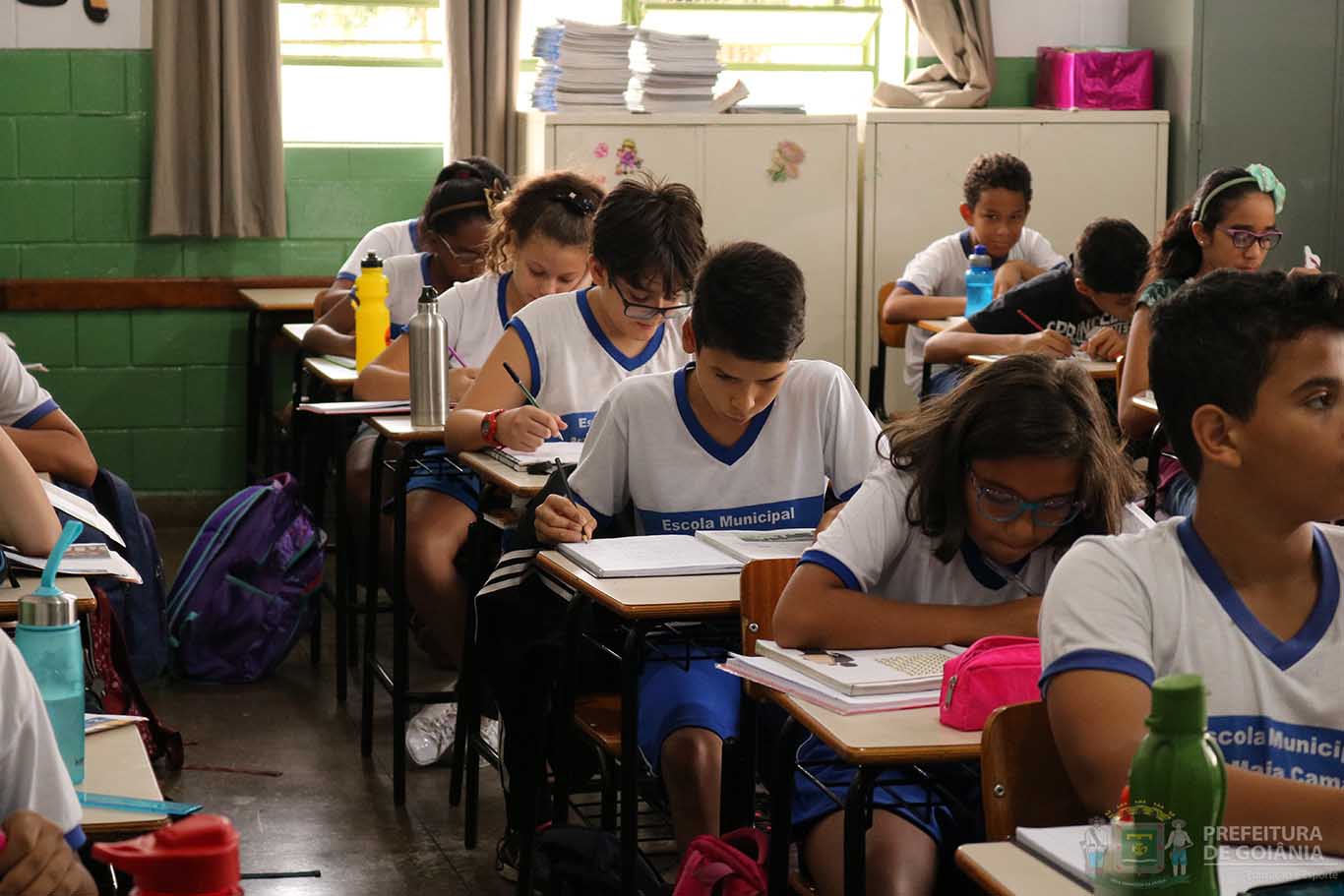 Alunos sentados em sala de aula escrevendo em seus cadernos