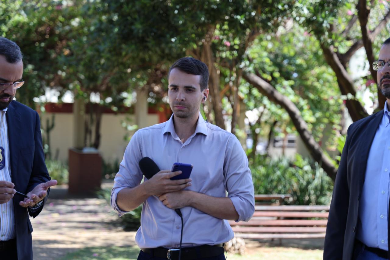 Imagem do repórter João Victor Guedes ao centro com um microfone na mão durante uma participação ao vivo na TV Anhanguera.
