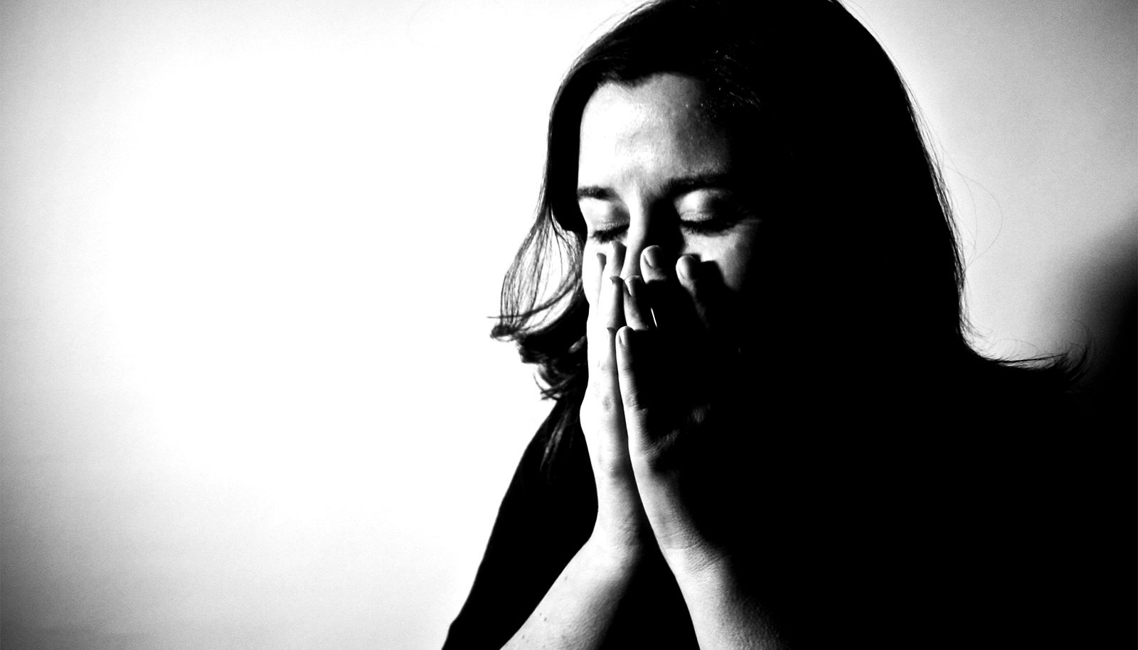 fotografia em preto e branco mostra mulher de olhos fechados tapando a boa com as mãos.