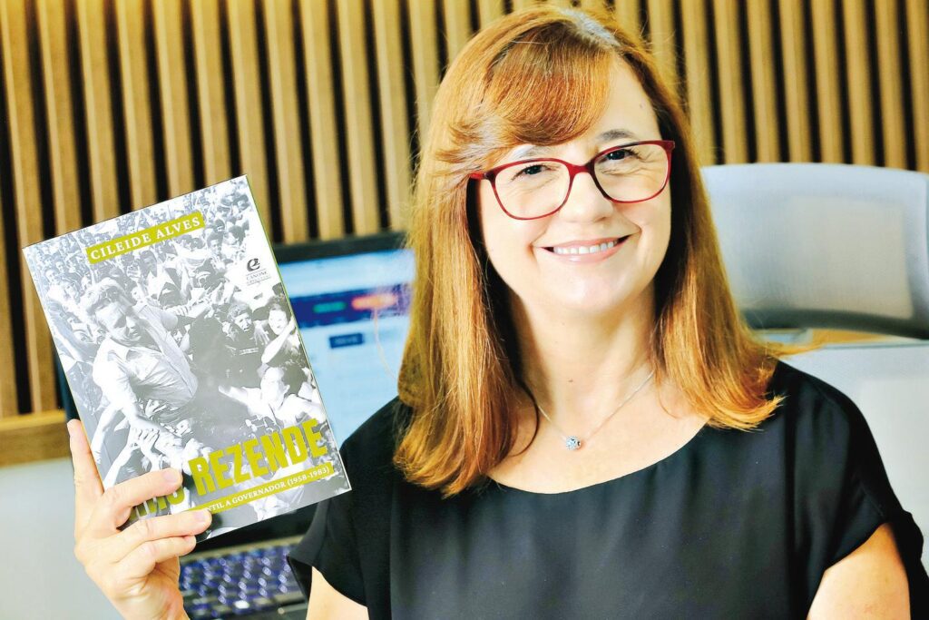 Foto da jornalista Cileide Alves segurando um livro.