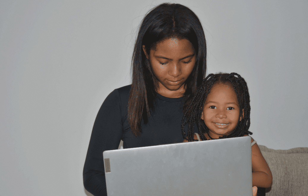 imagem mostra mulher negra utilizando notebook com a filha no colo